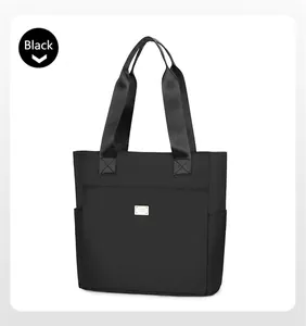 Detail of black nylon tote bag featuring wide shoulder straps and a central metal logo plate
