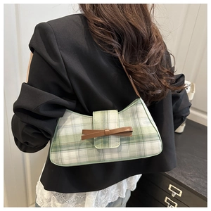 Model wearing a green plaid baguette bag with a brown leather bow and strap design