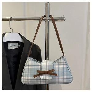 Close-up of blue plaid baguette bag with a brown leather bow and slim shoulder strap