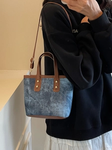 Sac bandoulière en denim bleu avec garniture en cuir marron porté par un mannequin