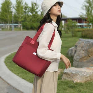 Asian model wearing a burgundy nylon tote bag with side pocket in an outdoor park setting