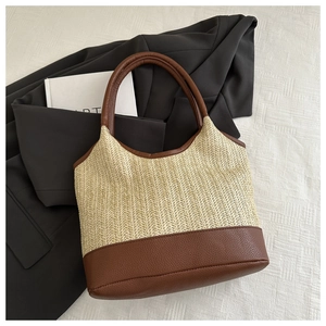 Close-up of woven straw tote bag with brown leather base and handle on white fabric