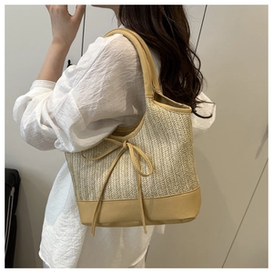 Detail view of large straw tote bag with khaki leather trim and bow on model