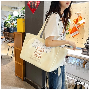 Detail of off-white corduroy tote bag featuring panda illustration and shoulder strap