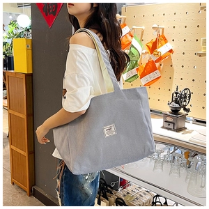 Detailed close-up showing the grey corduroy texture and white patch of the tote bag