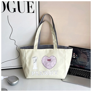 Close-up of off-white canvas tote bag featuring plush pink heart and grey webbing straps
