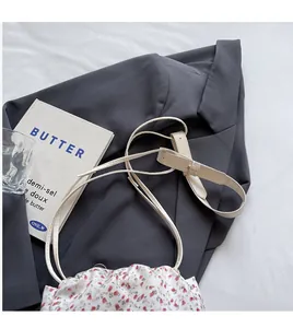 Detail of adjustable cream shoulder strap on floral canvas bag over grey suit fabric