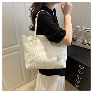 Detail of white quilted tote bag featuring vibrant butterfly embroidery and slim straps