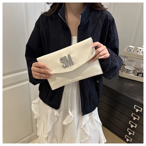 Close-up of cream glossy envelope clutch with rhinestone SM letter buckle detail