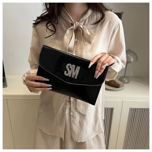Detail of a black patent leather envelope clutch with silver rhinestone SM initials