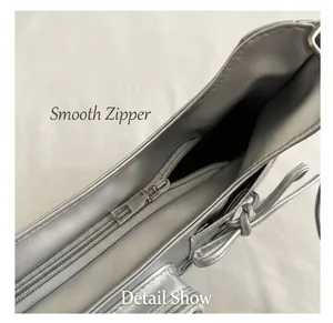 Detail of silver faux leather shoulder bag featuring a smooth metal zipper and denim background