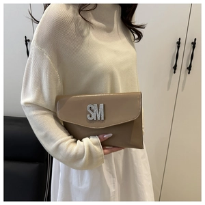 Detail of beige patent leather handbag with sparkling rhinestone SM logo held by hand