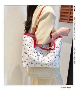 Macro shot of large cherry print tote bag featuring red handles and metal logo tag