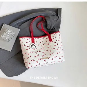 Detail of white cherry print tote bag with red handles and metal decorative trim
