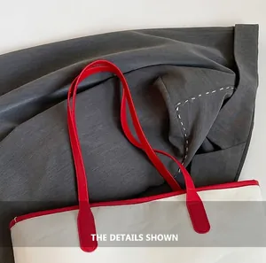 Detail of red leather handles and reinforced stitching on a large white tote bag