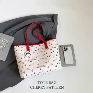 Detailed view of the red cherry print on white tote bag with a cartoon pendant