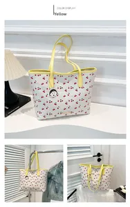 Detail of white cherry print tote bag with yellow handles and cartoon pendant accessory