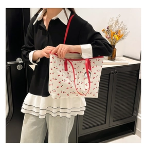 Detail of white cherry print tote bag with red straps and cute character pendant charm