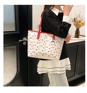 Detail of white tote bag with red cherry prints and a character charm accessory