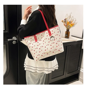 Close-up of white tote bag with red cherry print and character charm detail