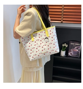 Detail of cherry print tote bag with yellow straps and cute character charm on handle