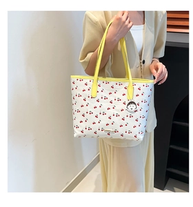 Detail of white tote bag with red cherry prints and yellow straps on a model