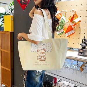 Large cream canvas panda tote bag with plush graphic shown in a cozy cafe setting
