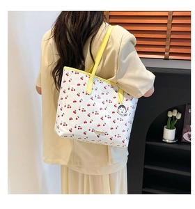 Detail of large white tote bag with red cherry print, yellow handle and gold logo plate
