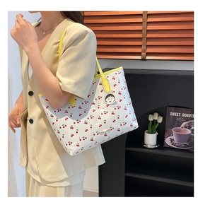 Close-up of white tote bag with red cherry prints and bright yellow shoulder strap detail