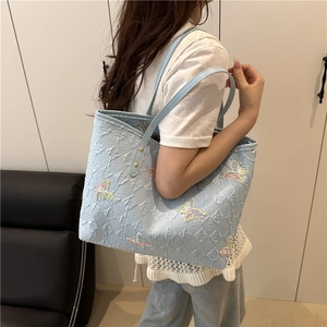 Blue tote bag with butterfly patterns and embossed E lettering on model shoulder