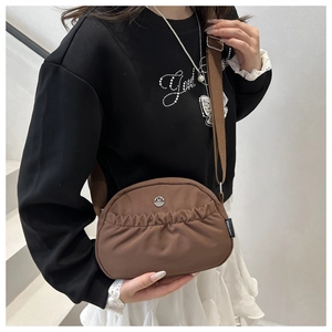Detail of a brown nylon crossbody bag featuring pleated fabric and a round silver logo