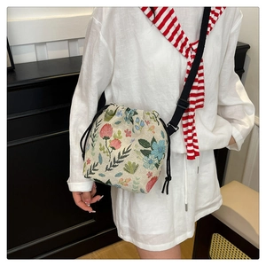 Detail of floral embroidery on a beige woven drawstring bucket bag with a long strap
