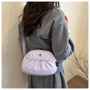 Detail of lavender canvas shoulder bag with pleated front pocket and round metal logo buckle