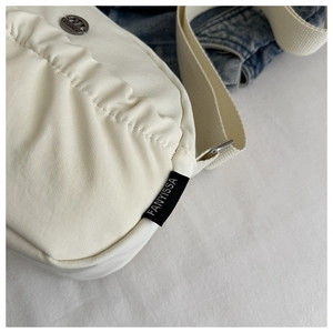 Detail of off-white pleated fabric bag with silver metal ornament and brand tag