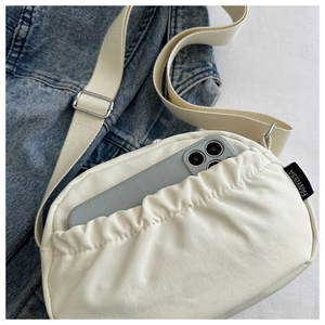 Detail of off-white crossbody bag featuring a pleated front pocket and a mobile phone inside