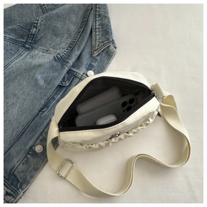 Detail of pleated crossbody bag interior with phone and accessories on denim