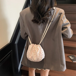 Floral drawstring bucket bag in cream and red, shown as a crossbody on a model