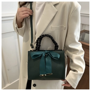 Detail of dark green square handbag with satin bow and braided handle on model