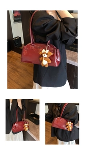 Detail of burgundy oil-waxed leather handbag with plush bear charm and glossy finish