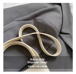 Détail d'une bandoulière réglable en cuir grainé blanc sur un fond de veste grise