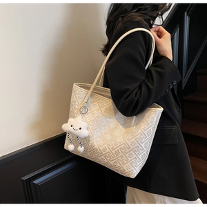 Detail of cream tote bag with geometric patterns and a plush cloud charm on a model