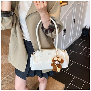 Detail of a creamy white waxed leather handbag with a cute brown teddy bear keychain