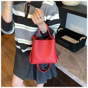 Détail du sac seau rouge en cuir grainé litchi avec une poignée fine élégante