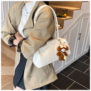 Close-up of white glossy shoulder bag with logo embossing and a cute plush bear pendant