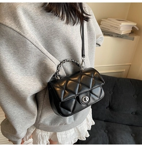 Sac bandoulière noir matelassé avec chaîne argentée et fermoir rotatif porté par un mannequin