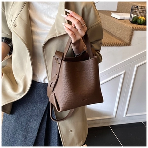 Gros plan du sac seau en cuir grainé marron avec poignée et détails de sangle