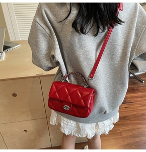 Détail du sac bandoulière matelassé rouge avec fermoir argenté porté par le mannequin