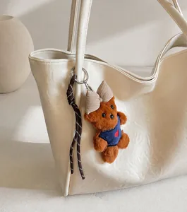 Detail of a brown plush bear charm with a blue heart vest on a beige tote bag