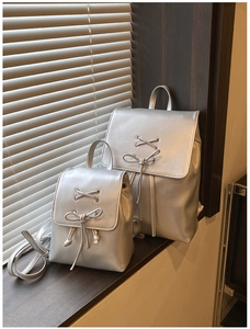 Silberne Metallic-Rucksäcke mit dekorativen Schleifen auf einem sonnigen Holzfensterbrett