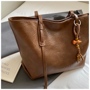 Close-up of brown tote bag showing supple leather texture and wooden gourd charm